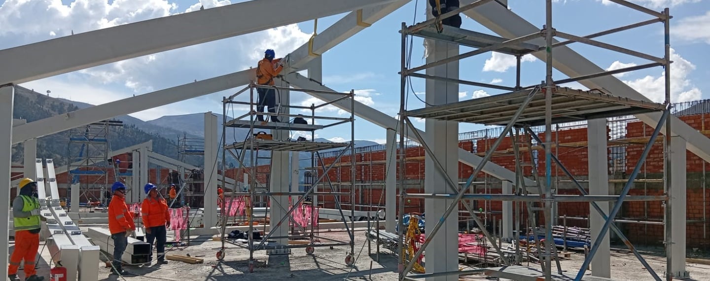 Construction workers in safety gear install steel beams and scaffolding at an industrial building site.