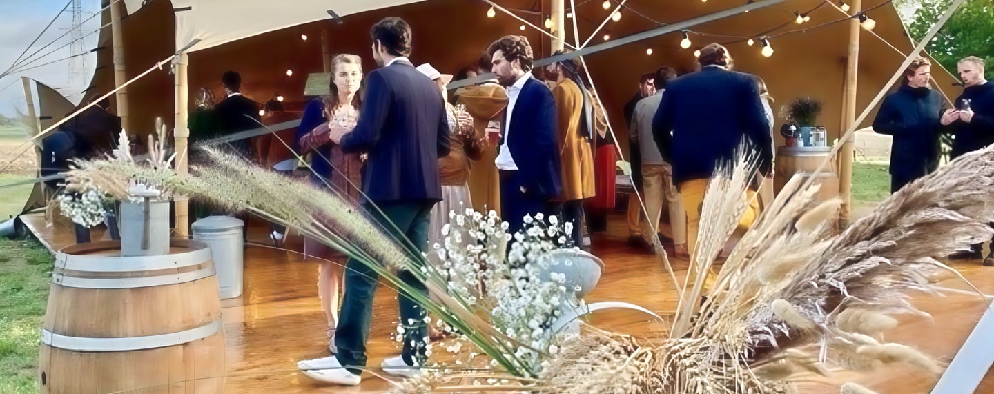 Invités discutant sous une tente stretch décorée de tonneaux, lors d’un mariage
