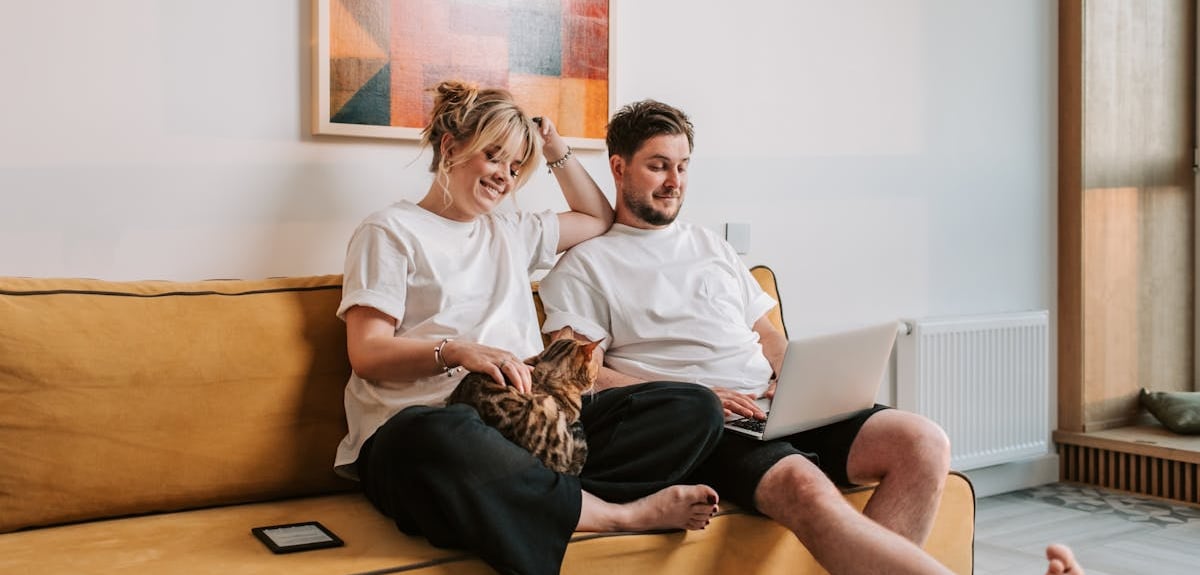 A couple sitting on sofa with their cat and reading about cat vomiting with no other symptoms on the