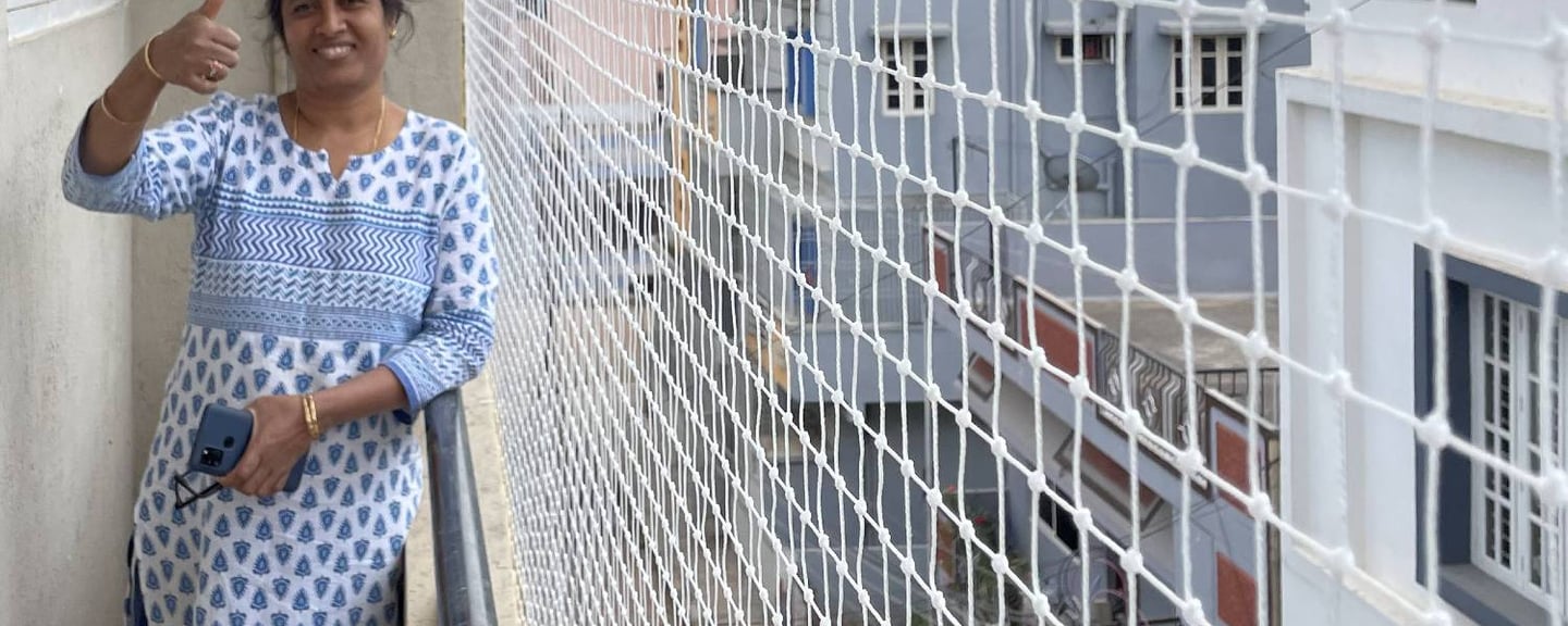A technician carefully fitting a white pigeon net on a modern apartment balcony in Whitefield.