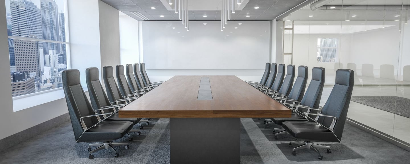A sleek conference room with a large projection screen, long wooden table, and high-back chairs