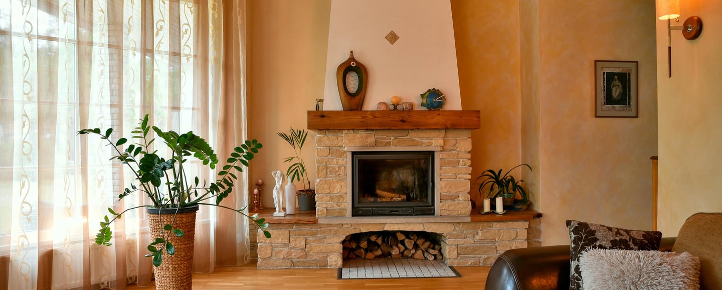 Light stone fireplace with wood storage inside luxury home. Large window and plant to the left