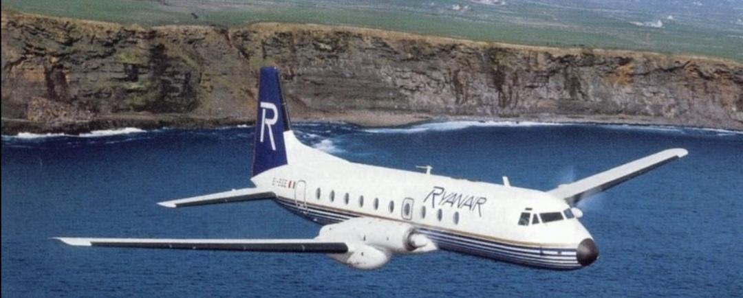 Vintage Ryanair propeller airplane flying over the ocean near steep coastal cliffs.