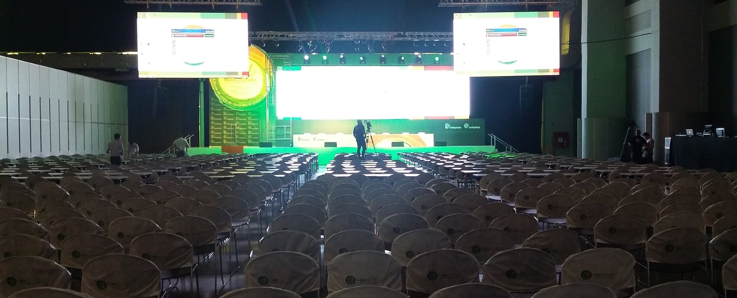 Empty conference hall with rows of chairs facing a stage with bright LED screens for a corporate event.