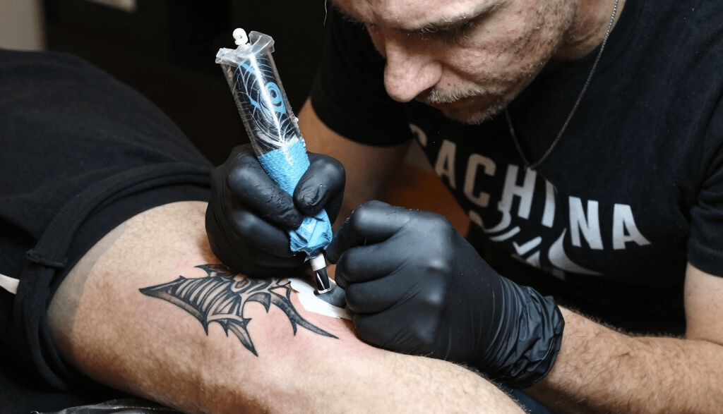 Close-up of a tattoo artist working meticulously on a client's skin in a neon-lit studio.