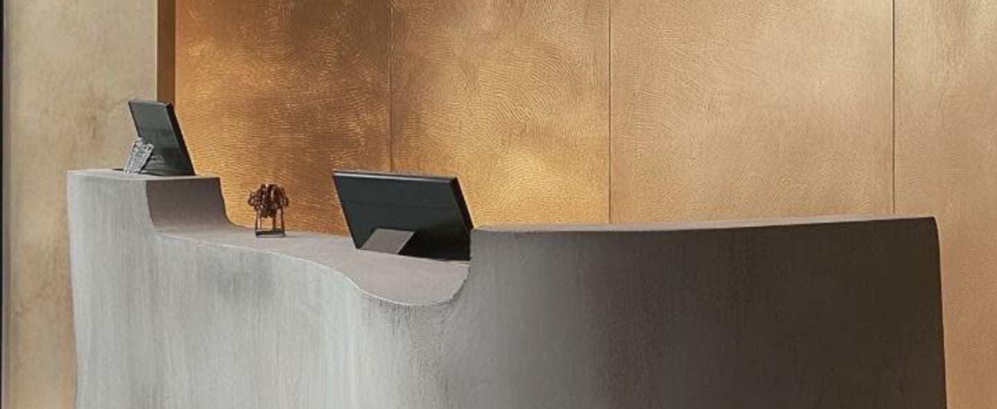 A modern reception desk with computer monitors, set against a microcement wall