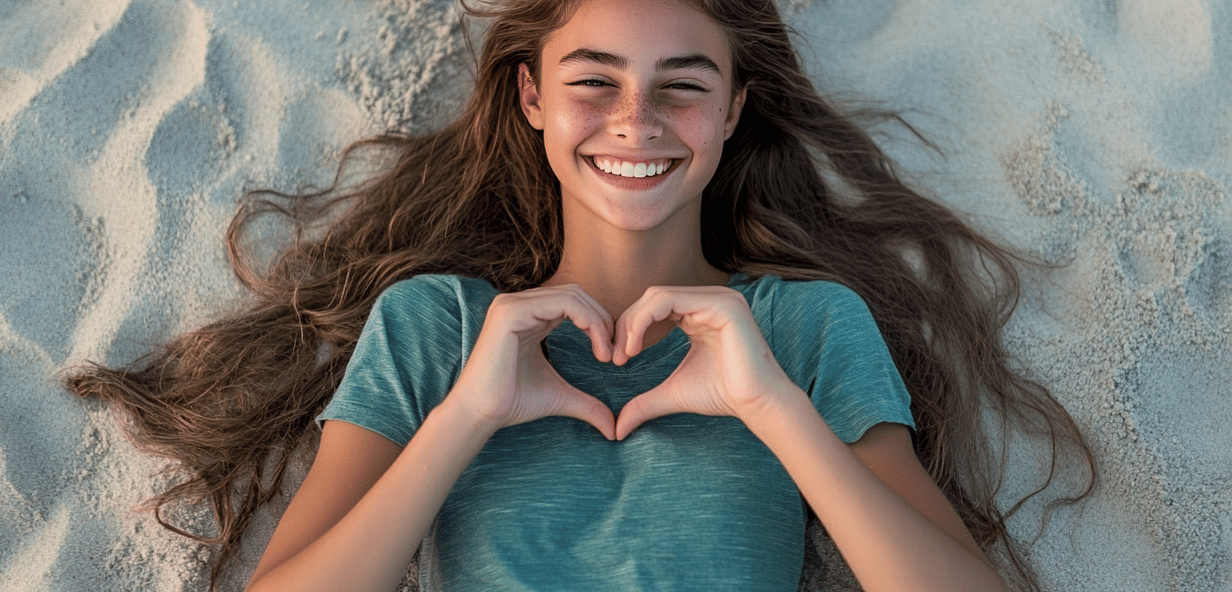 Adolescente recostada sobre arena haciendo un corazon con sus manos 