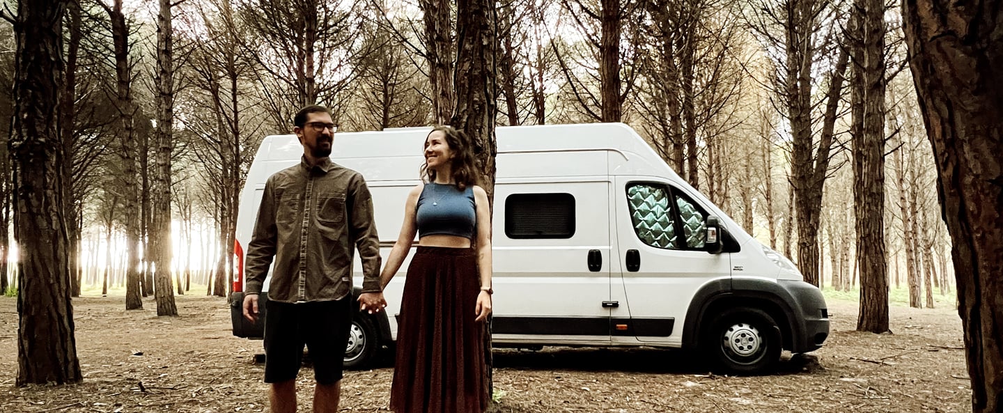 casal sorrindo na floresta em frente a um motorhome