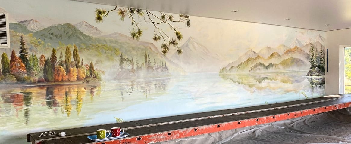 Painted panorama lake mural in progress with scaffold, showing New Zealand mountains and water view.
