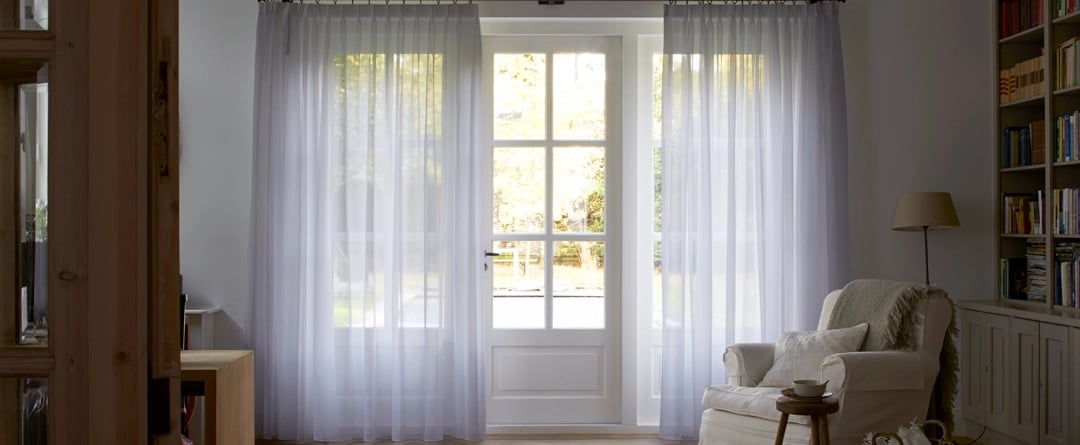 Grands rideaux tamisants blanc devant de larges fenêtres dans une entrée avec fauteuil et tapis
