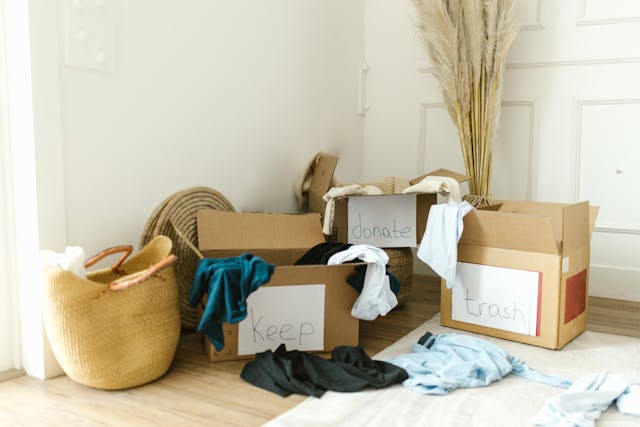 Clothing decluttering and home organization using cardboard boxes labeled keep, donate, and trash.