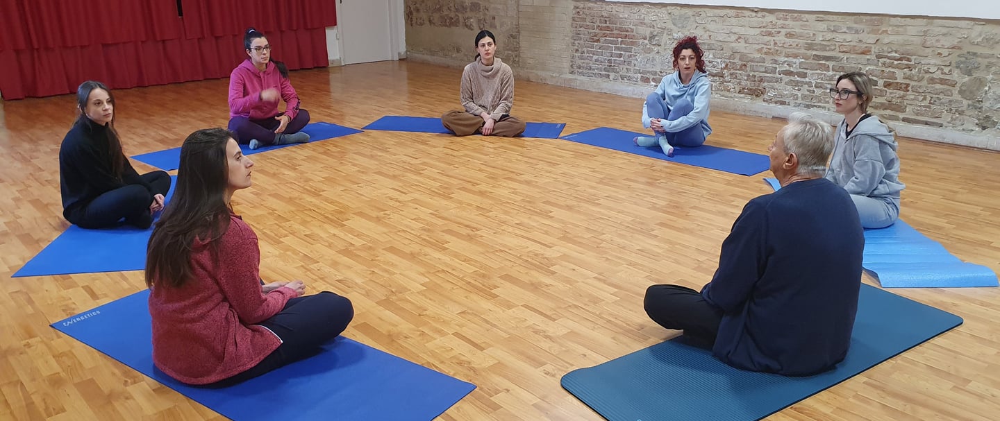 a group of people sitting on yoga mats in a circle, classe di esercizi di bioenergetica