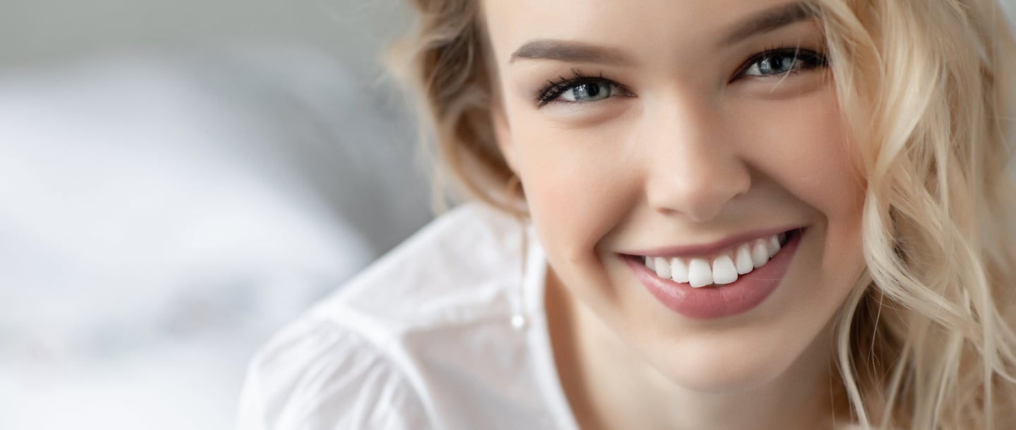 A blonde woman with a bright smile showcasing white teeth and healthy skin in a portrait.