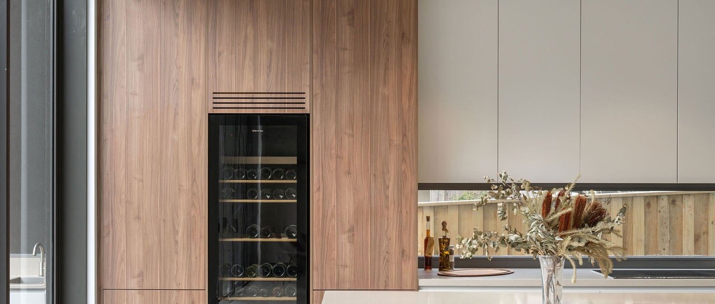 Nowoczesna jasna kuchnia. W wysokiej szafce zamontowana przeszklona lodówka na wino