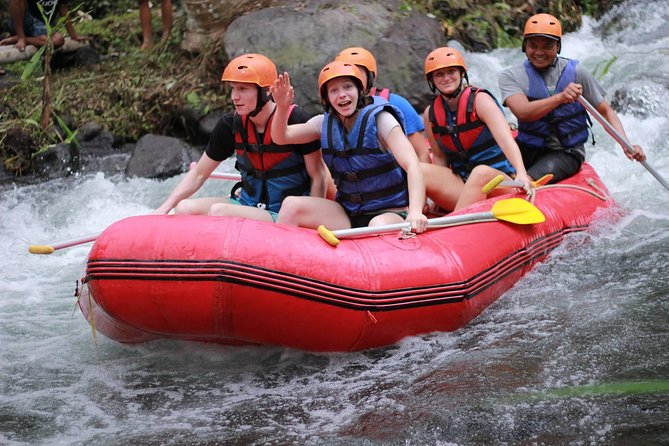 A group of cheerful tourists wearing life jackets and helmets on a white water rafting adventure in a red boat.