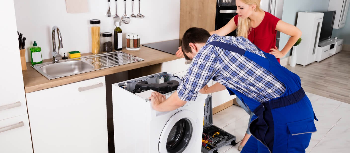 a man and woman working on a washing machine