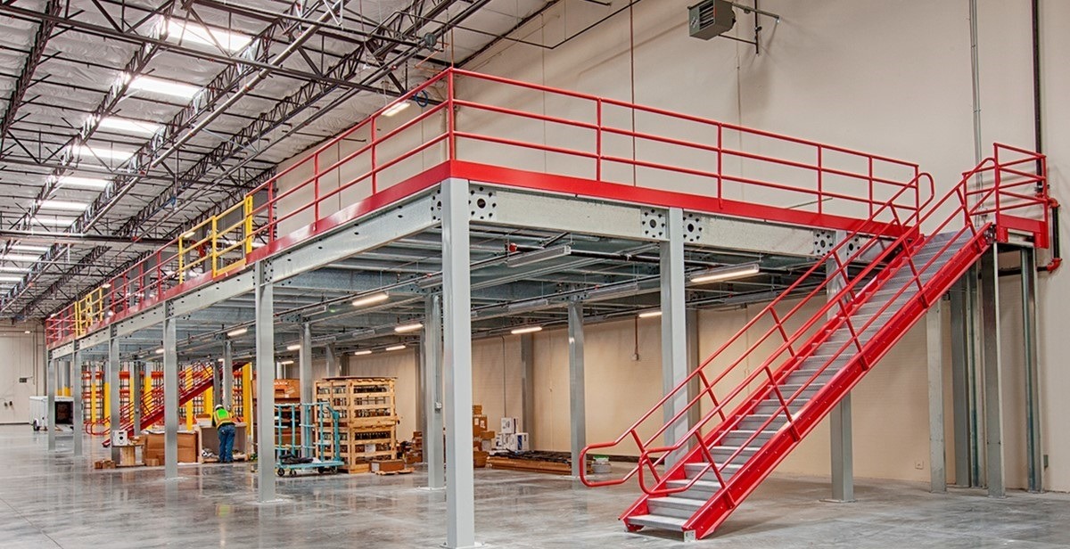 Industrial warehouse mezzanine floor with red safety handrails and steel staircase for storage.