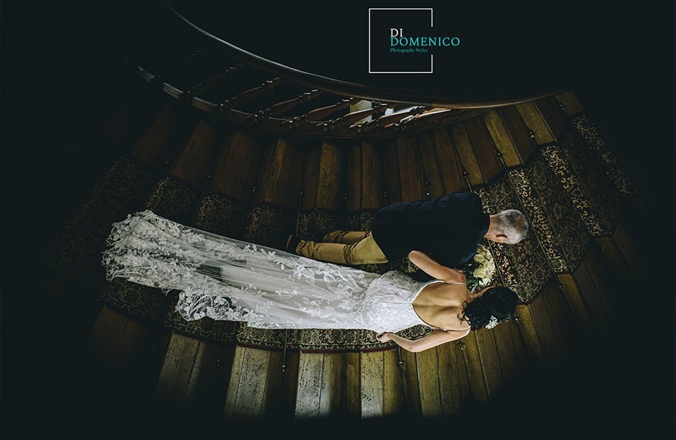 Mariés descendant un escalier en colimaçon vue d’en haut, robe dentelle et costume noir.