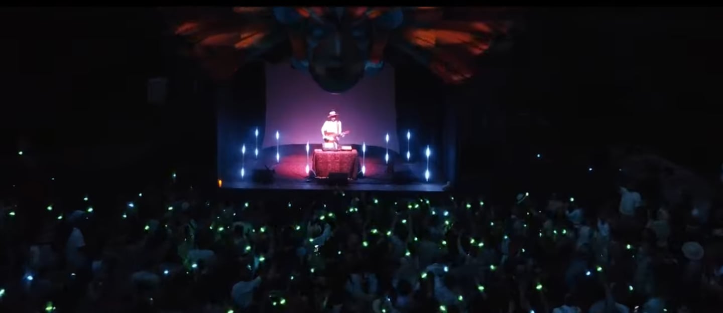 Musician performing live on a concert stage with glowing green lights from the crowd.