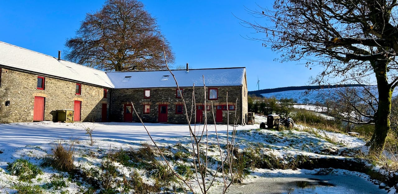 A large barn with a pond and in the snow with bright winter sunlight