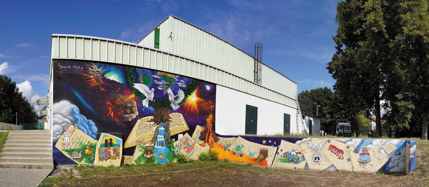 Vibrant outdoor wall mural on a white building featuring peace doves, space themes, and open storybooks.
