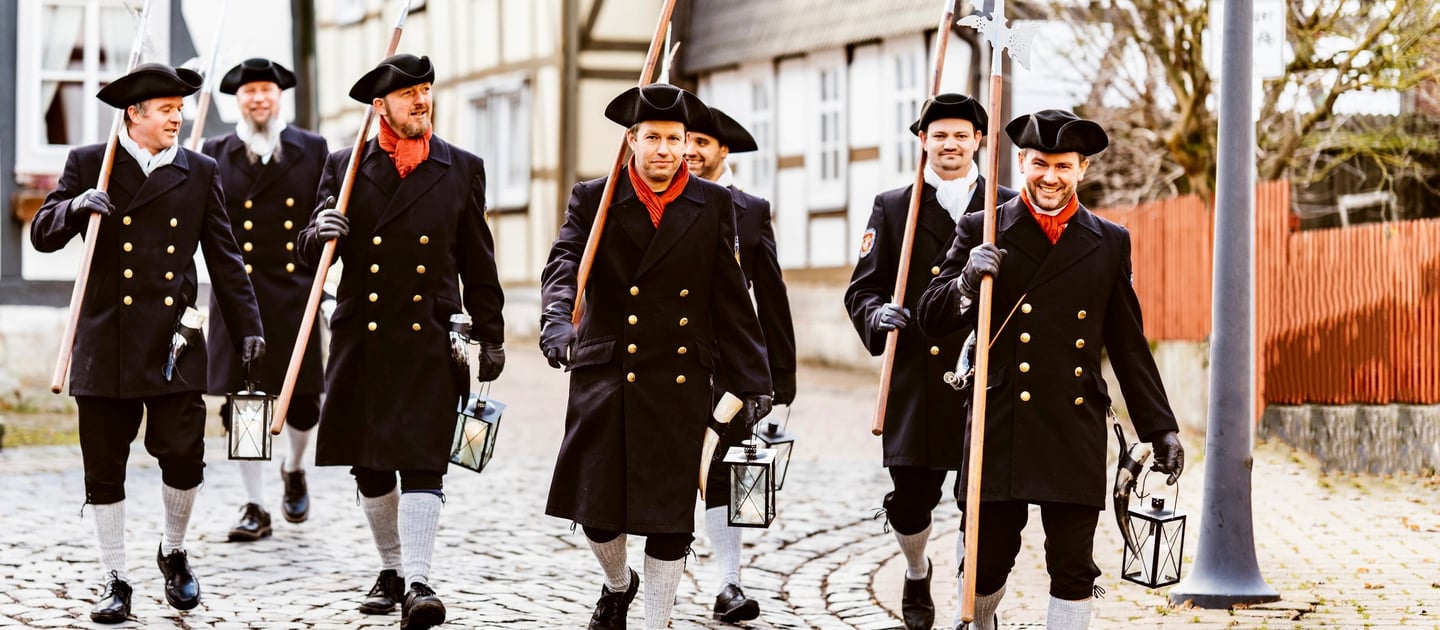 a group of men in uniform uniforms walking down a cobblestone