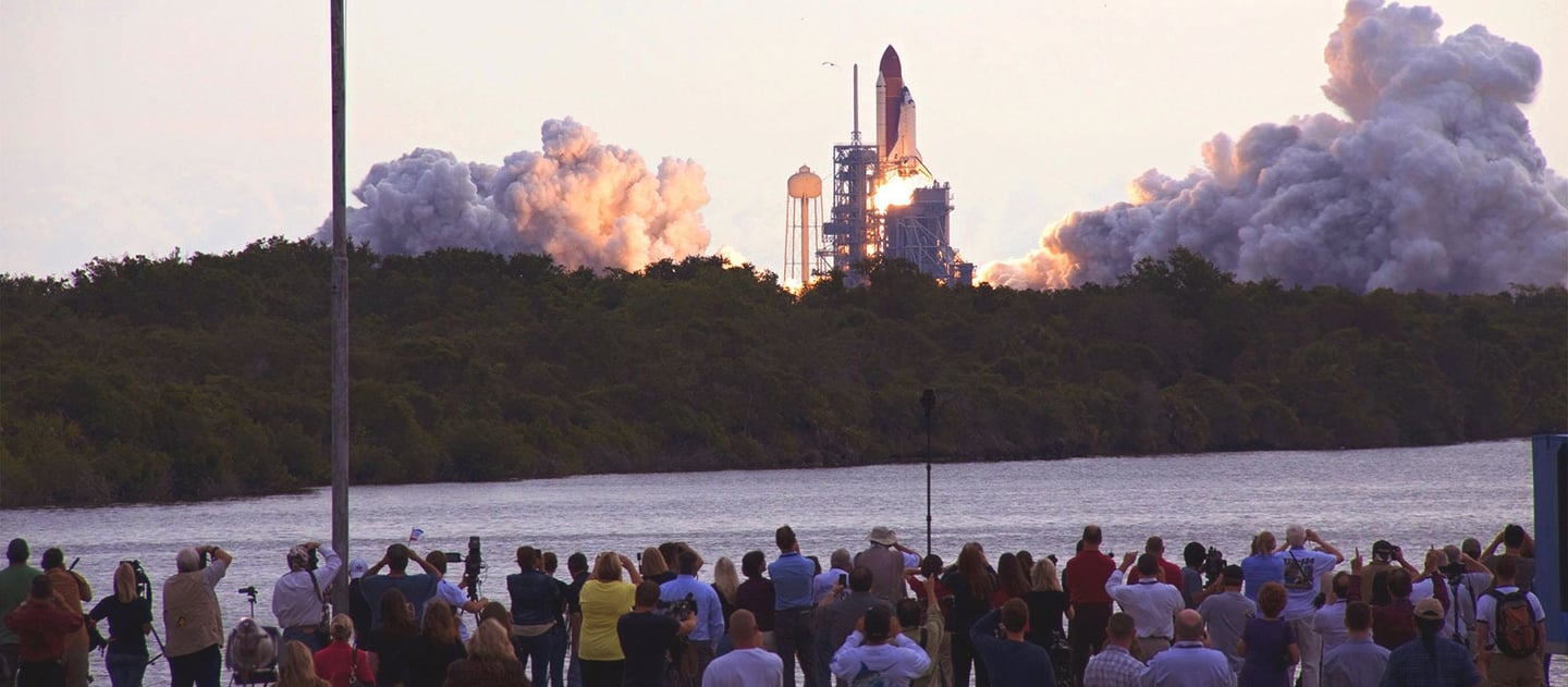 toma abierta de muchas personas mirando y tomando fotos hacia el despegue de una nave espacial