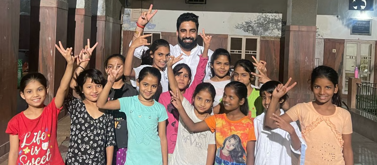 Vikash Sharma with a group of cheerful young girls making peace signs at a school or community center