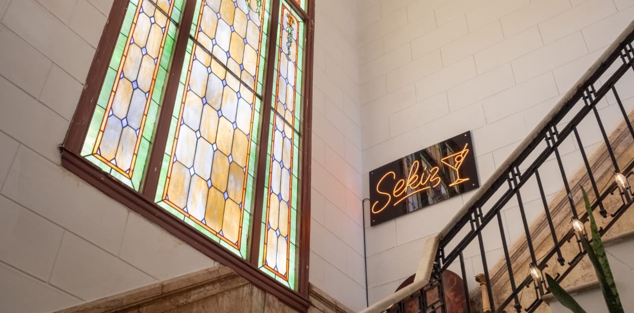 Vintage interior staircase featuring a large stained glass window and Sekiz neon cocktail sign.