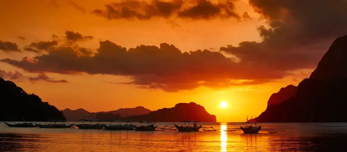 Traditional boat sailing in El Nido bay during a golden sunset dinner cruise