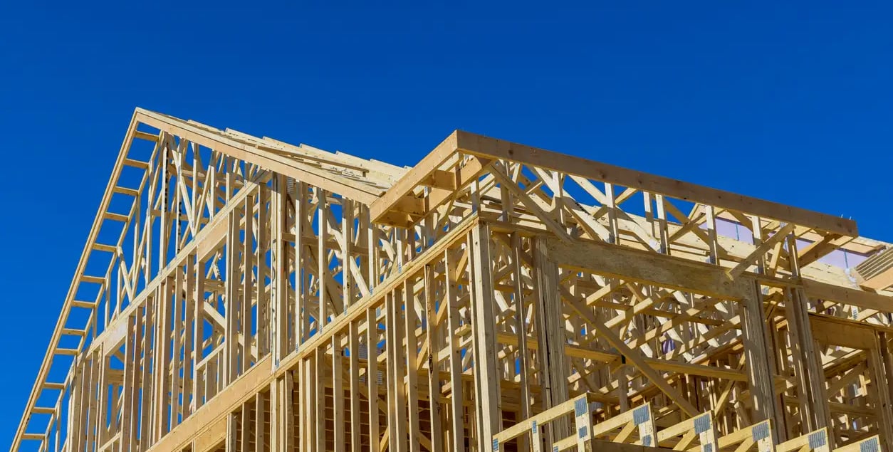 Wooden frame of a new residential house under construction against a clear blue sky.