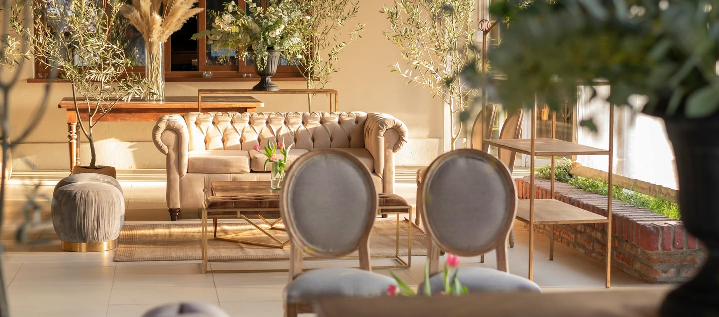 Luxury white chesterfield lounge in a well lit room surrounded by plants and other white furniture