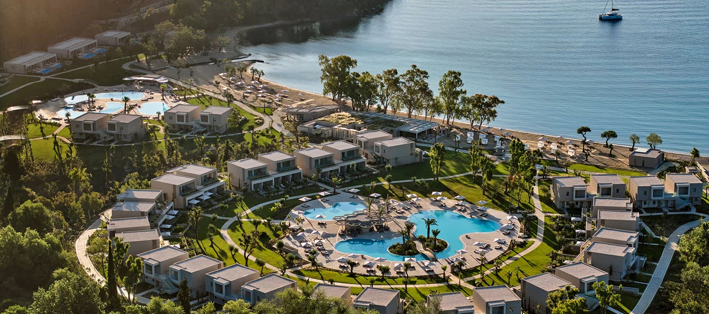 Aerial view of a luxury beachfront resort with circular swimming pools and private villas near the ocean.