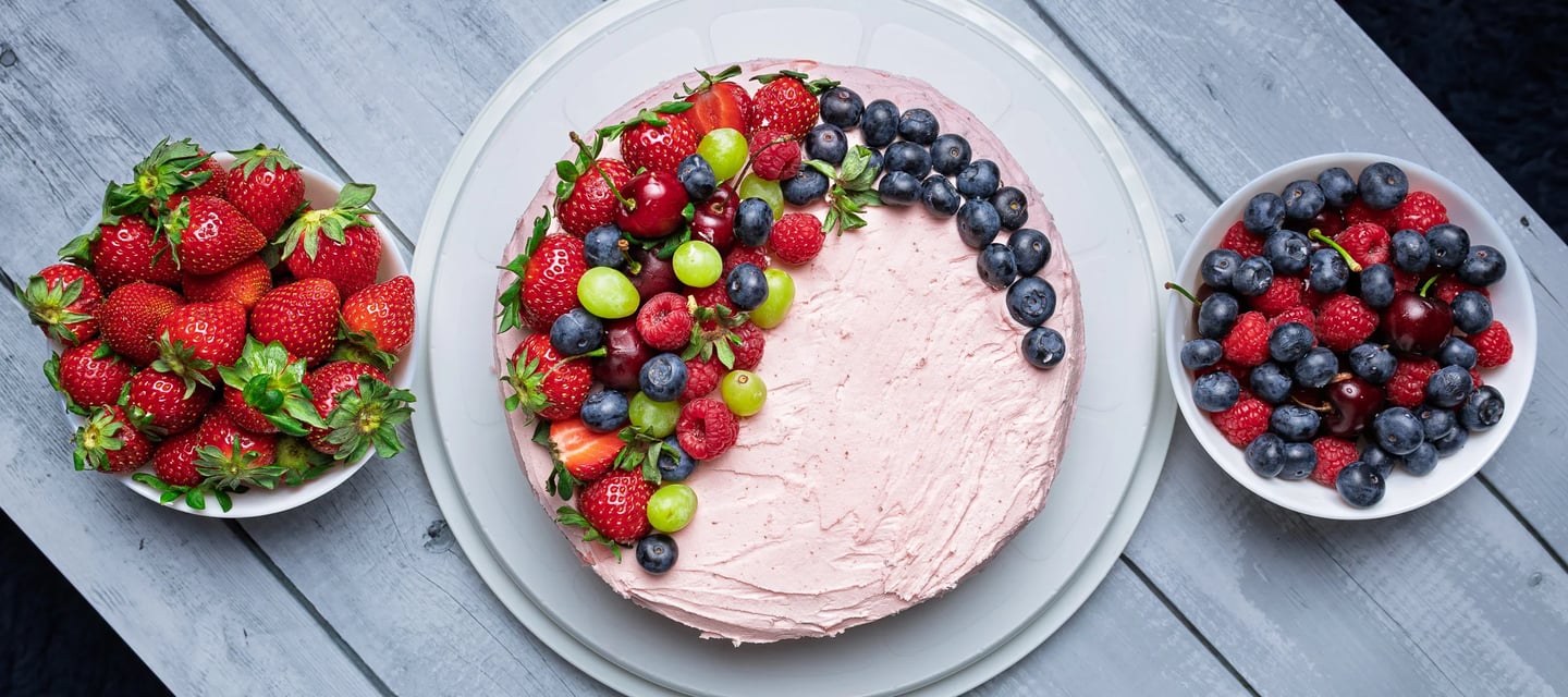 a cake with fruit on a table with bowls of fruit
