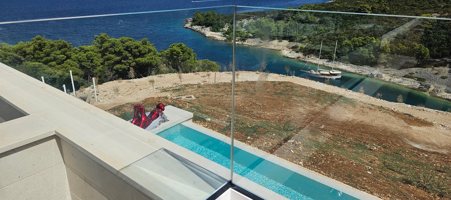 Staklena ograda balkona sa pogledom na uvalu i more