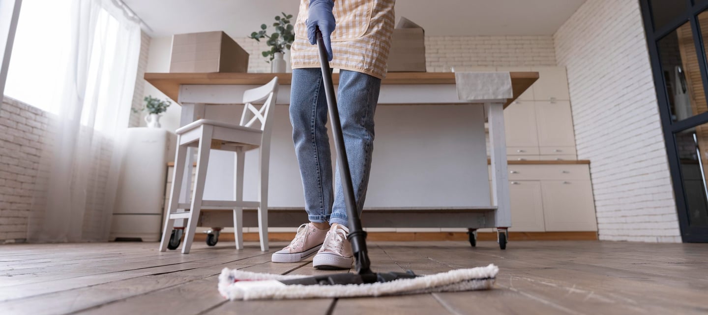 a woman in a pink shirt and jeans cleaning a wooden floor