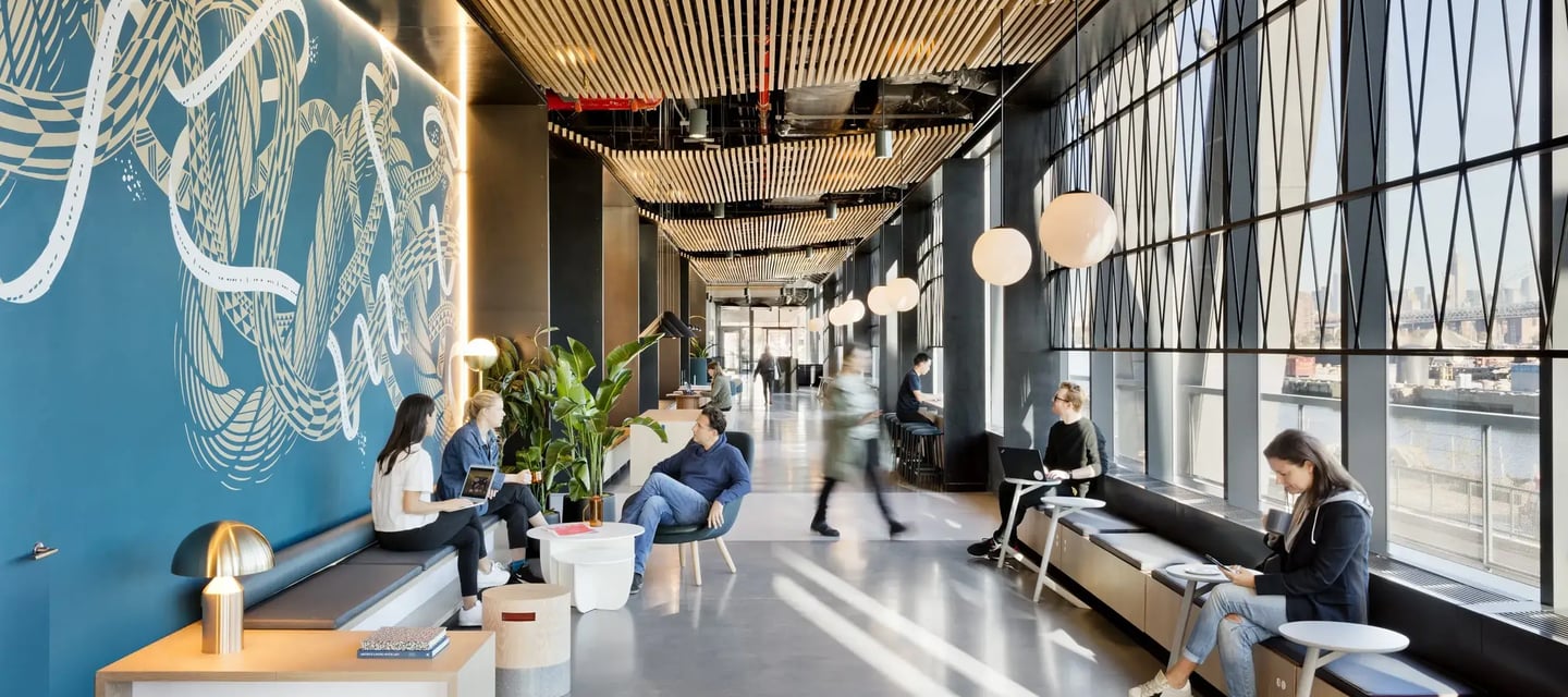 Modern office breakout area with wood slat ceilings, mural wall, and people working in a bright lounge.