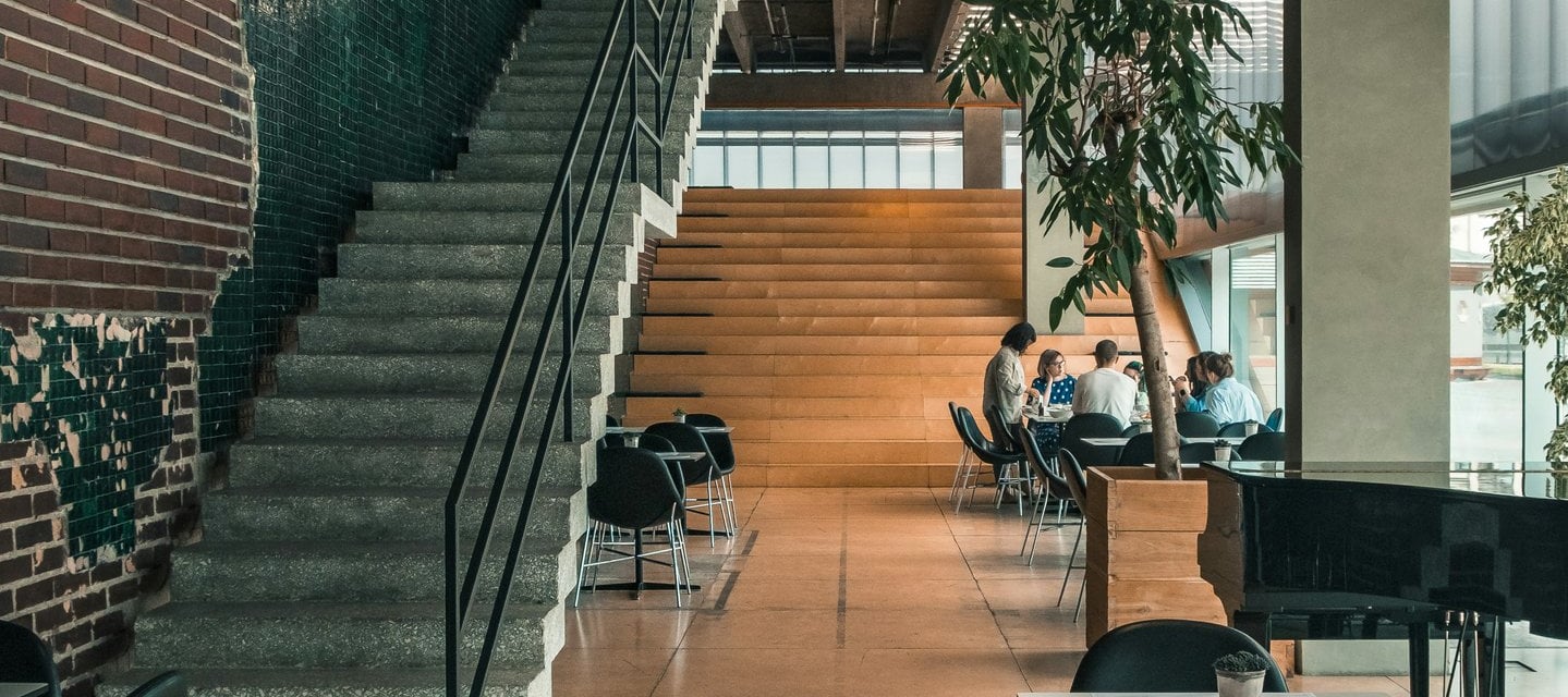 Modern industrial cafe interior with concrete stairs, brick walls, and people sitting at tables.