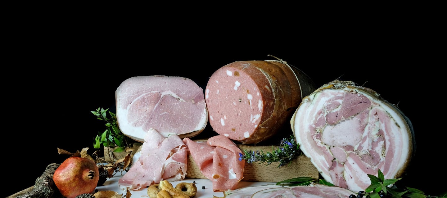 Variety of Italian cured meats including mortadella, prosciutto, and porchetta with garnishes.