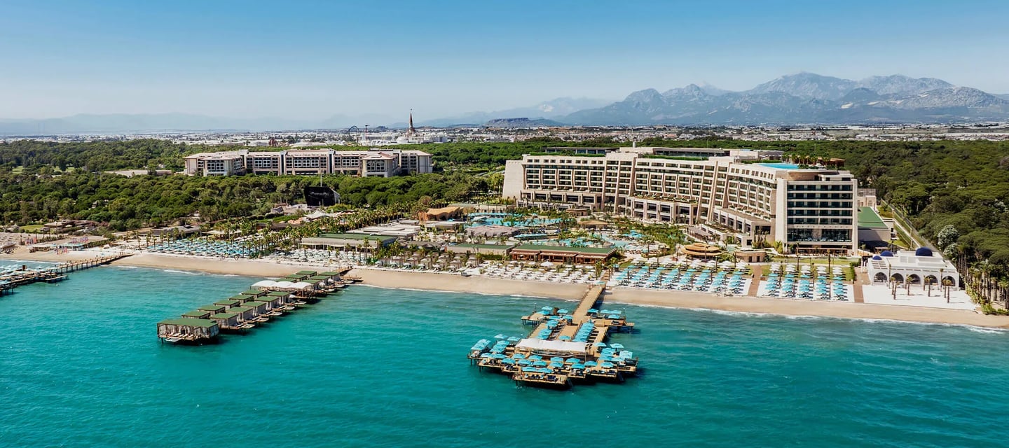 Regnum The Crown, Belek resort in Turkey with piers, blue water, and mountains.