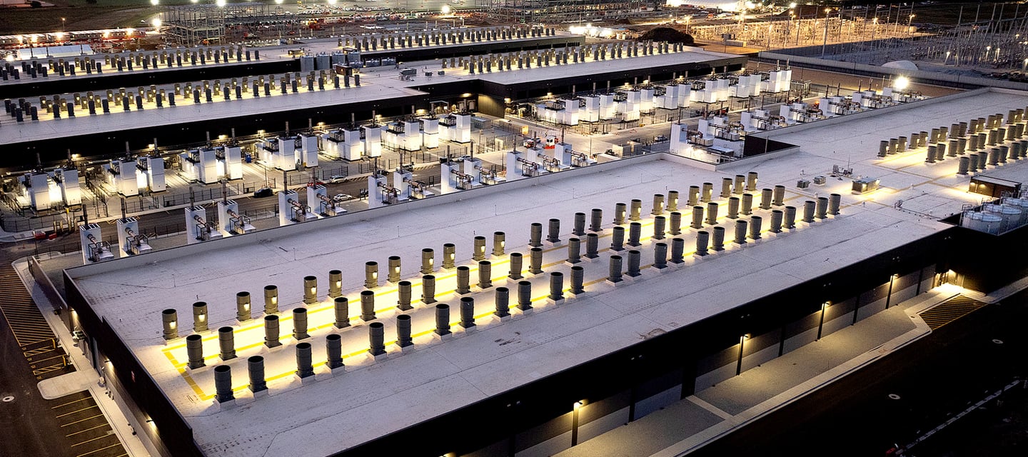 Aerial night view of a large-scale data center facility with industrial cooling systems and illuminated infrastructure.