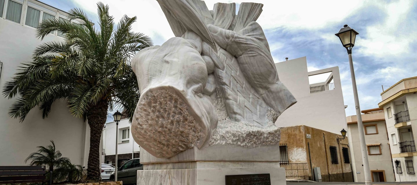 White marble sculpture of hands weaving a rope braid on a pedestal in a city square.