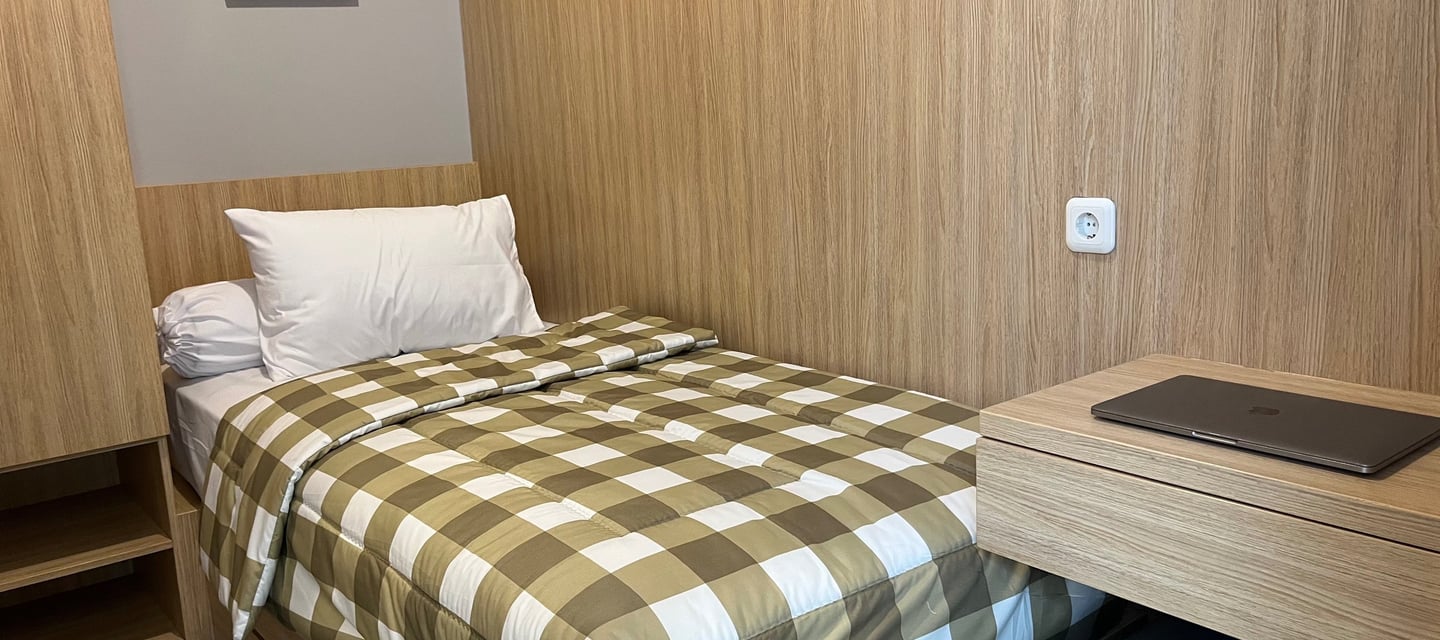 Kamar kos eksklusif Kos Si Bos Surabaya dengan single bed, meja belajar, lemari kayu, dan suasana modern minimalis