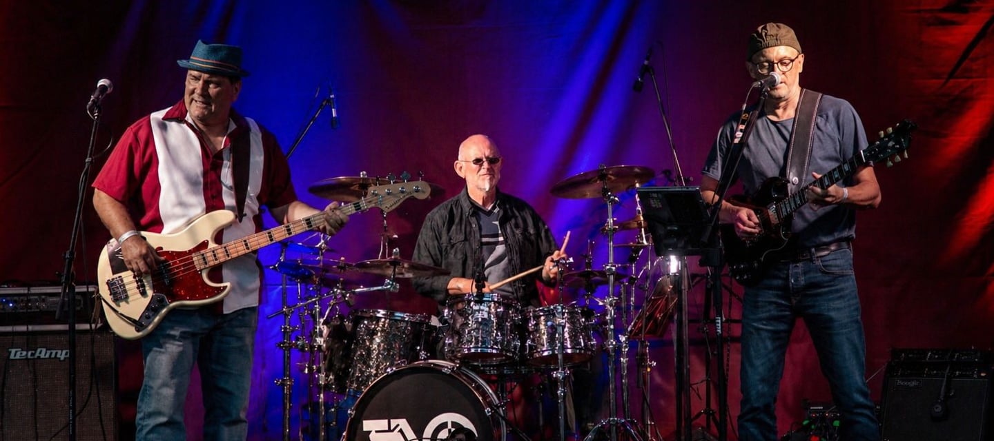 Live Bluesrock-Band performt auf der Bühne mit Drummer, Bassist und Gitarrist mit buntem Licht