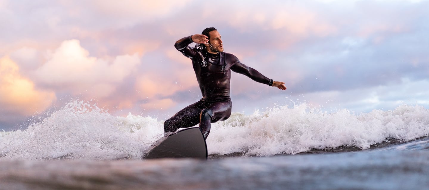 a man in a wetsuit surfing on a surfboard on sunset