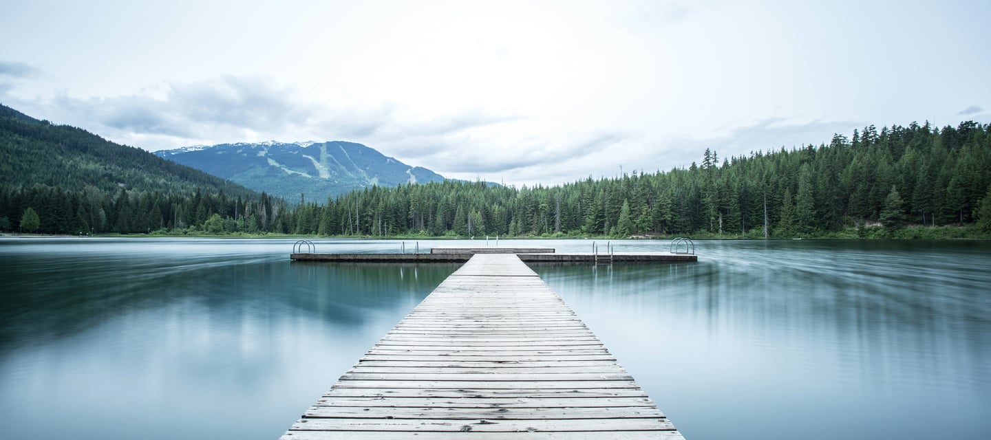 Cais em meio à floresta, com montanhas ao fundo.