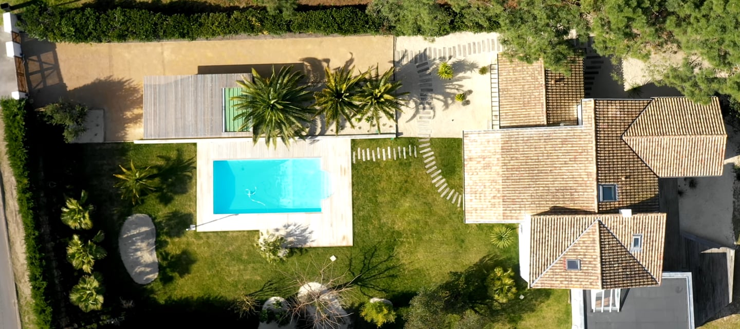 Vue aérienne d'une villa de luxe avec une piscine turquoise, pelouse verte manucurée et palmiers.