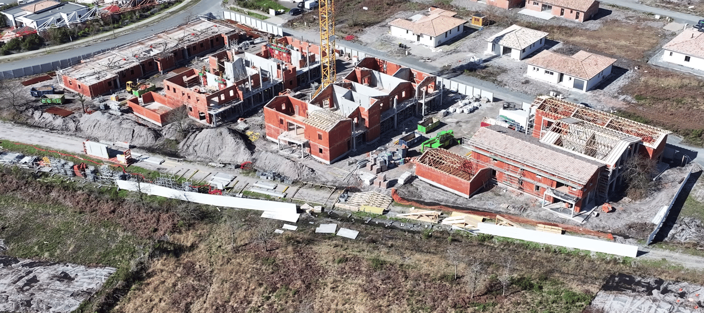 Vue aérienne d'un chantier résidentiel avec maisons en briques et une grue à tour jaune.