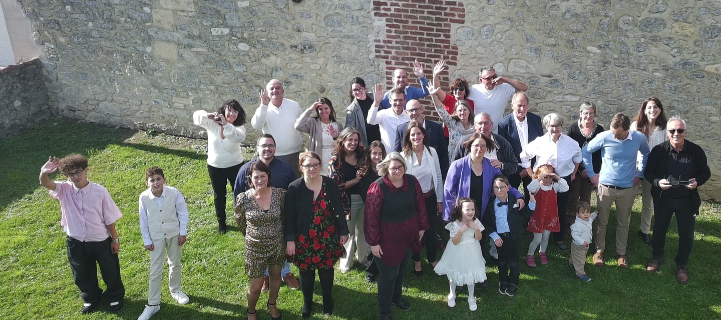 A large multi-generational group of people waving and smiling for a family photo outdoors.