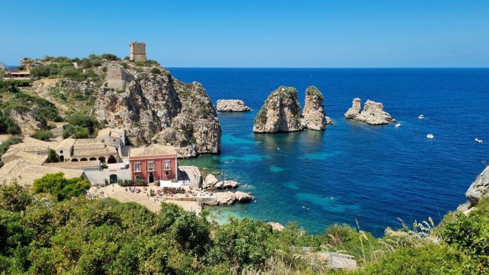 Panoramic view of Tonnara di Scopello featuring coastal rock stacks and the historic tower in Sicily.
